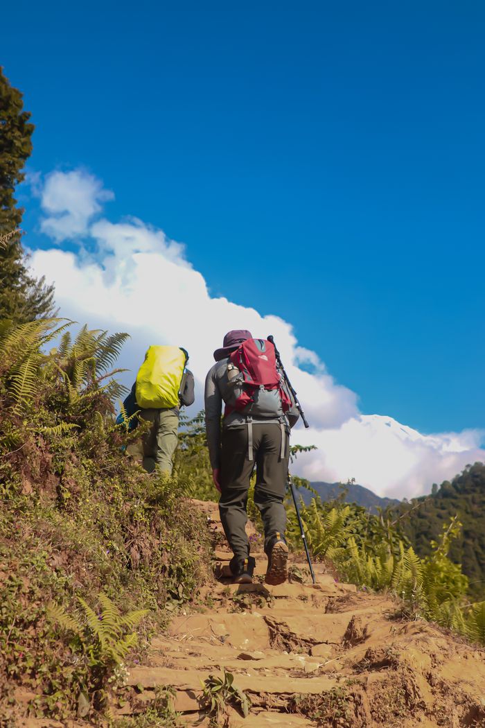 Two adults hiking a scenic trail in Annapurna, Nepal with backpacks and trekking poles.